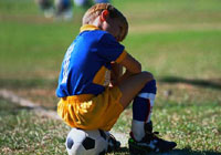young soccer player sitting on the soccer ball on the sidelines